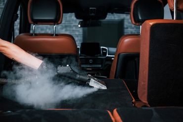 A technician from Bang Bang  is cleaning the back seat of a car with a vacuum cleaner.