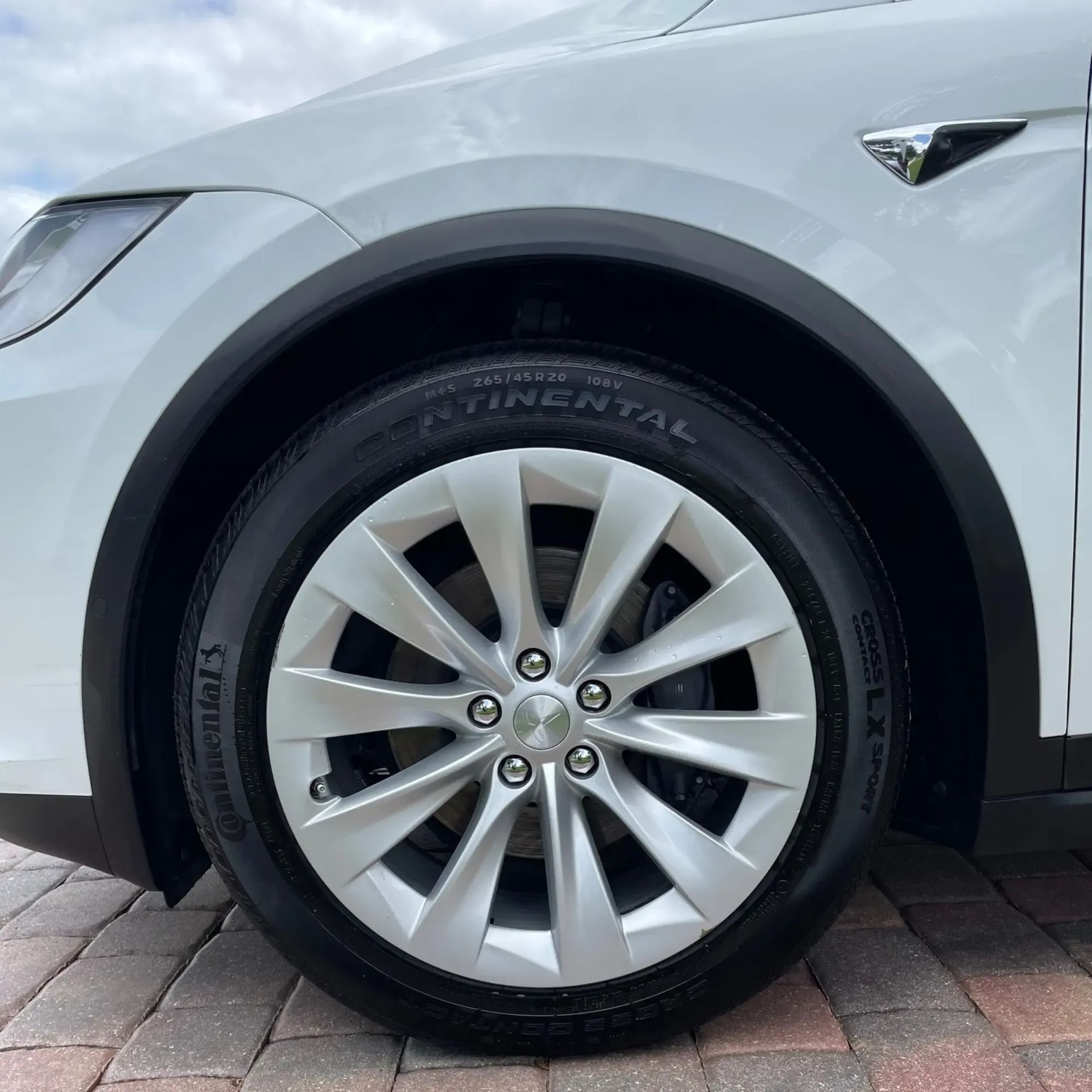 A white tesla model s is parked on a brick sidewalk